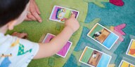 Ein Kind hockt auf einem bunten Spielteppich und zeigt auf eine Spielkarte.