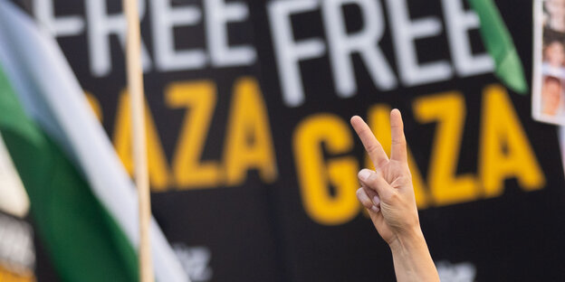 Eine Hand macht der Victory-Zeichen vor „Free-Gaza“-Plakaten
